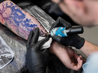 Close-up of tattoo needle applying ink to vibrant multicolored landscape arm piece