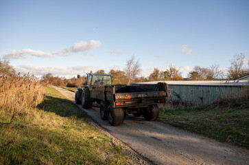 Obraz premium tractor with trailer driving on rural dirt road in autumn countryside