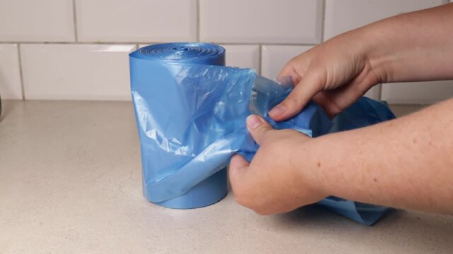 hands tearing a blue trash bag from a roll on a kitchen counter demonstrating a basic household task related to waste management and everyday cleaning routines