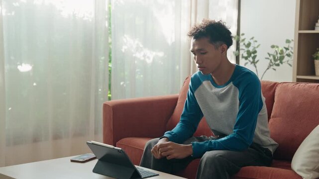Asian teenage man learning sign language via internet with technology on tablet at home