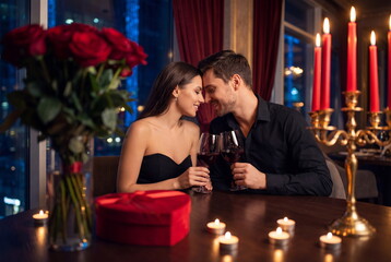Romantic couple toasting with wine, touching foreheads during a candlelight dinner. Valentine's day with roses and gift in a luxury restaurant