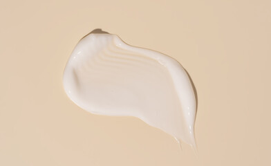 Squeezed cosmetic white cream texture isolated on beige background. Close up spf or cream, mask drop smear