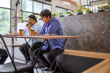 Two young professionals collaborate on project with laptops and coffee in bright modern cafe