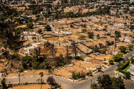 Aerial view of wildfire-damaged residential lots in Southern California showing empty foundations, brown terrain, and ongoing land clearing and reconstruction