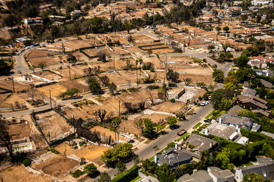 Aerial view of wildfire-damaged residential lots in Southern California showing empty foundations, brown terrain, and ongoing land clearing and reconstruction
