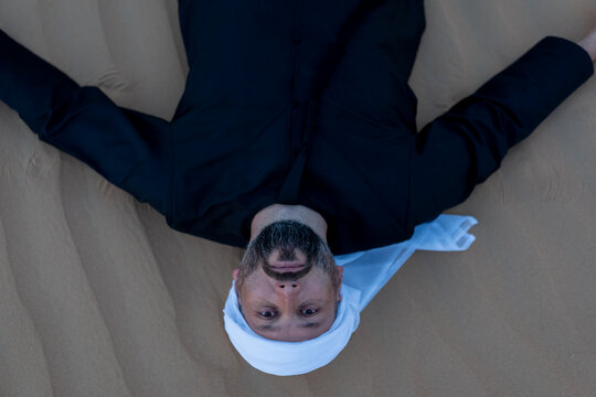 Relaxing male tourist wearing traditional arab clothing, lying on desert sand dunes. High quality photo