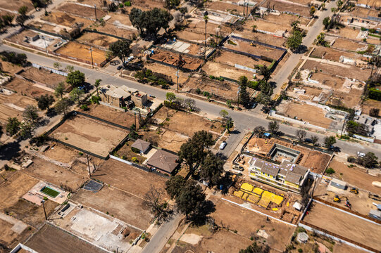 Aerial view of wildfire-damaged residential lots in Southern California showing empty foundations, brown terrain, and ongoing land clearing and reconstruction