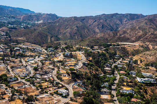 Aerial view of suburban neighborhoods beside wildfire-damaged lots in Southern California, contrasting green residential areas with scorched brown terrain