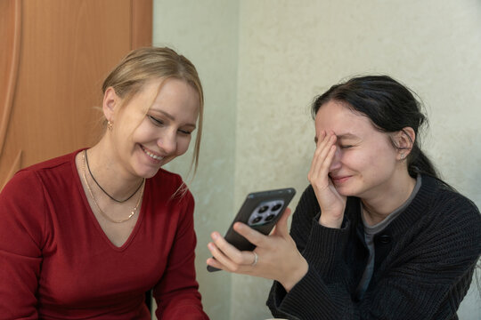 Friends laughing while looking at a smartphone screen in a cozy indoor moment