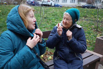 Two elderly ladies, mother and daughter, are walking in the park on an autumn day, talking and laughing.