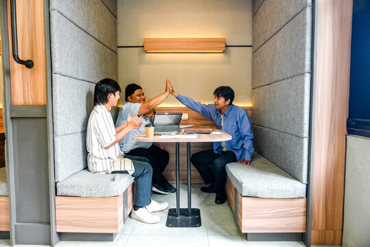 Dynamic team celebrating success with high five in modern collaborative workspace