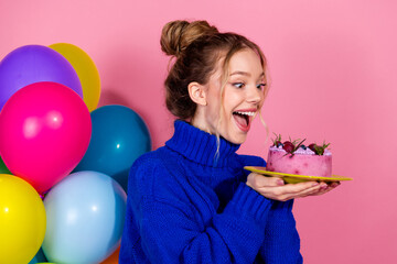 Young woman in blue sweater holds pink berry cake with balloons against pink backdrop at...