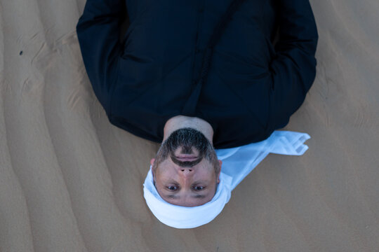 Relaxing male tourist wearing traditional arab clothing, lying on desert sand dunes. High quality photo