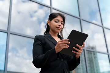 Business professional using a tablet outside a modern office building on a sunny day
