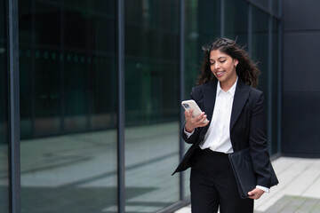 Businesswoman walking and checking her smartphone in a modern urban setting during the day