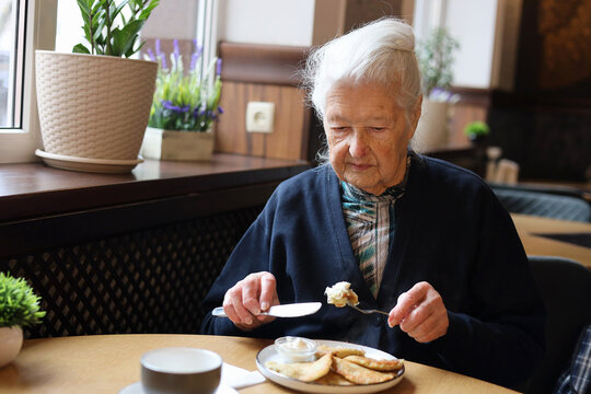 Portrait of a 90-year-old grey haired senior lady dining in a restaurant. Soup, main course, tea. Conversation.