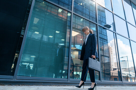 Businesswoman in formal attire walks confidently past a modern office building on a sunny day in the city