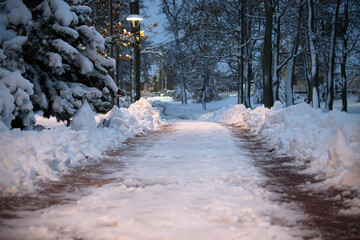 Snowy Park Path at Dusk with Lamplight and Snow Piles Along the Walkway