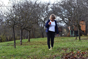 Woman walking outdoors in an orchard with a red mug
