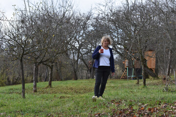 Woman walking outdoors in an orchard with a red mug