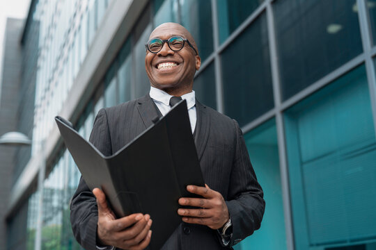 Business professional smiling outdoors while holding a portfolio outside a modern office building