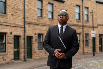Business professional in formal attire stands thoughtfully outside historic stone buildings in a...