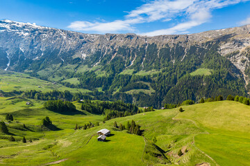 Alpe di siusi with dolomites, alpine lush green meadows. Mountains in background. Aerial view. Wooden barns in alpine meadow © Leonid