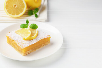 Tasty lemon bar with powdered sugar and mint on white wooden table, closeup. Space for text