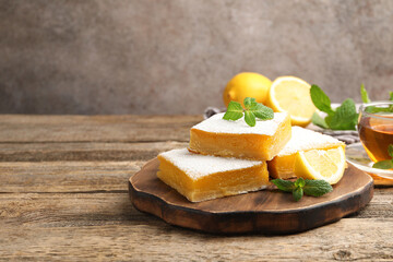 Tasty lemon bars with mint, fresh fruits and tea on wooden table, closeup. Space for text