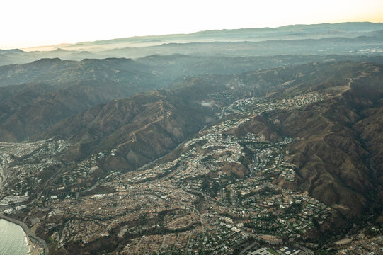 Aerial view of hillside residential neighbourhoods and sports fields in Los Angeles County, California, showing dry mountain terrain and suburban grid patterns on a clear sunny day