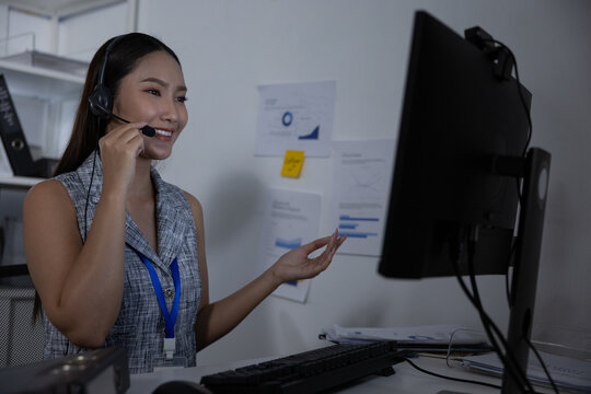 Friendly customer service representative wearing headset and lanyard smiling while assisting client at computer desk in office environment
