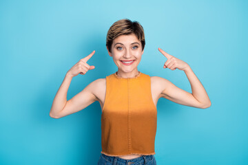 Fototapeta premium Happy stylish young woman with short blonde hair pointing to her head against blue background in casual chic outfit
