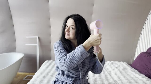 Adult woman drying her hair with a pink hair dryer at home, part of a daily beauty routine and hair care process, modern self-care, grooming habits, and healthy hair maintenance in a cozy home interio