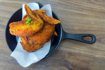 Crispy golden chicken wings rest in a small skillet, their surface glistening with a rich seasoning blend.