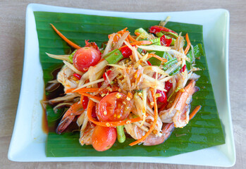 Papaya salad with fermented fish,cooked shrimp placed on a banana leaf and a white plate, very colorful and appetizing.