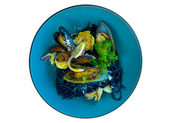 A vibrant seafood pasta featuring black squid-ink noodles topped with mussels, shrimp, and squid. The dish is garnished with fresh herbs and grated cheese.