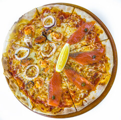 This is a seafood pizza topped with squid rings, mussels, shrimp, and slices of smoked salmon. A lemon wedge sits in the center, and the thin crust is evenly cut into slices.