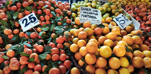 Fresh mandarins with leaves, oranges, and persimmons piled on Turkish market stall, handwritten price tags adding authentic rustic atmosphere. Culinary, lifestyle, and creative projects