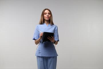 Young caucasian female nurse in blue scrubs holding digital tablet