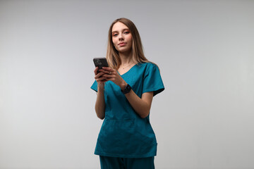 Naklejka premium Young caucasian female nurse using smartphone in scrubs against white background