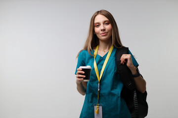 Young caucasian female nurse with coffee and backpack smiling confidently