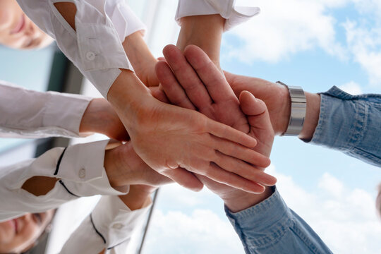 Team members joining hands in a circle to symbolize unity and collaboration during a project meeting outdoors