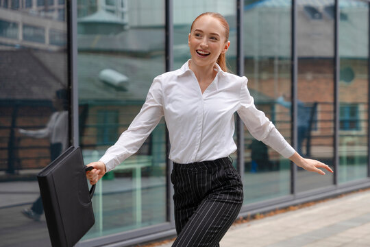 Young professional woman in business attire walking confidently with a briefcase on city sidewalk - Powered by Adobe