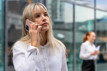 Young woman talks on smartphone while another professional looks on in a busy urban setting