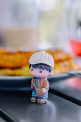 Close-up vertical shot of a cute mini figure on a table. Blurred food background, travel concept