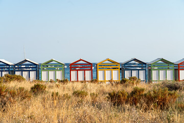 Row of colorful wooden beach huts on sea bathing beach behind tall, dry grass. S'Agarò Banys near Tossa de Mar, Costa Brava, Spain. Colourful summer Mediterranean background.