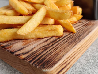 Golden crispy French fries on old wooden board on table in cafe. Potatoes lightly sprinkled with salt. Close-up.