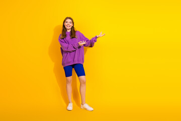 Young woman in purple hoodie and blue shorts smiles against bright yellow background for fashion lifestyle image