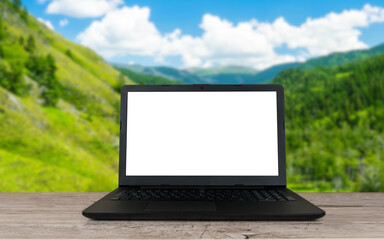 open laptop with blank screen on wooden table and summer mountains or hills blurred background, remote or distant work place, vacation working concept, travel blogging template
