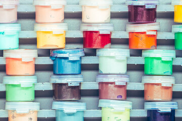 a close-up view of numerous small, translucent plastic containers filed with a vibrant assortment of colorful paints likely gouache or acrylic, neatly stacked in rows. The bright, vivid hues.